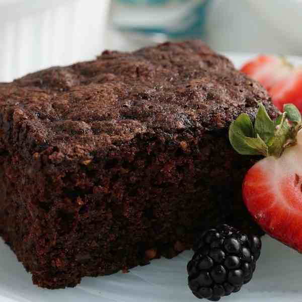 a slice of moist chocolate zucchini cake with some strawberries and a blackberry
